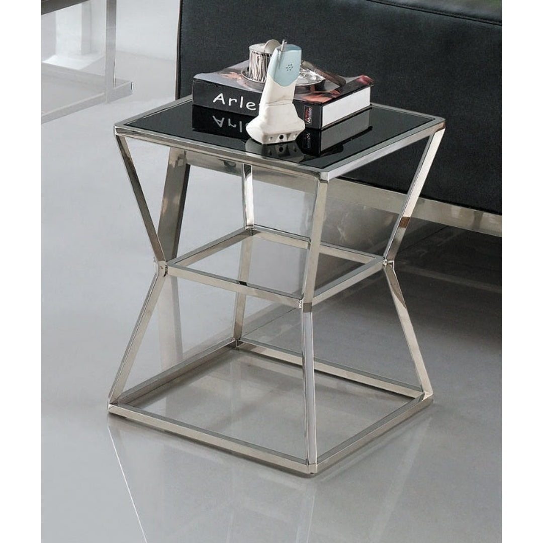 A polished stainless steel side table with black tempered glass top, with items placed on top in a showroom setting.