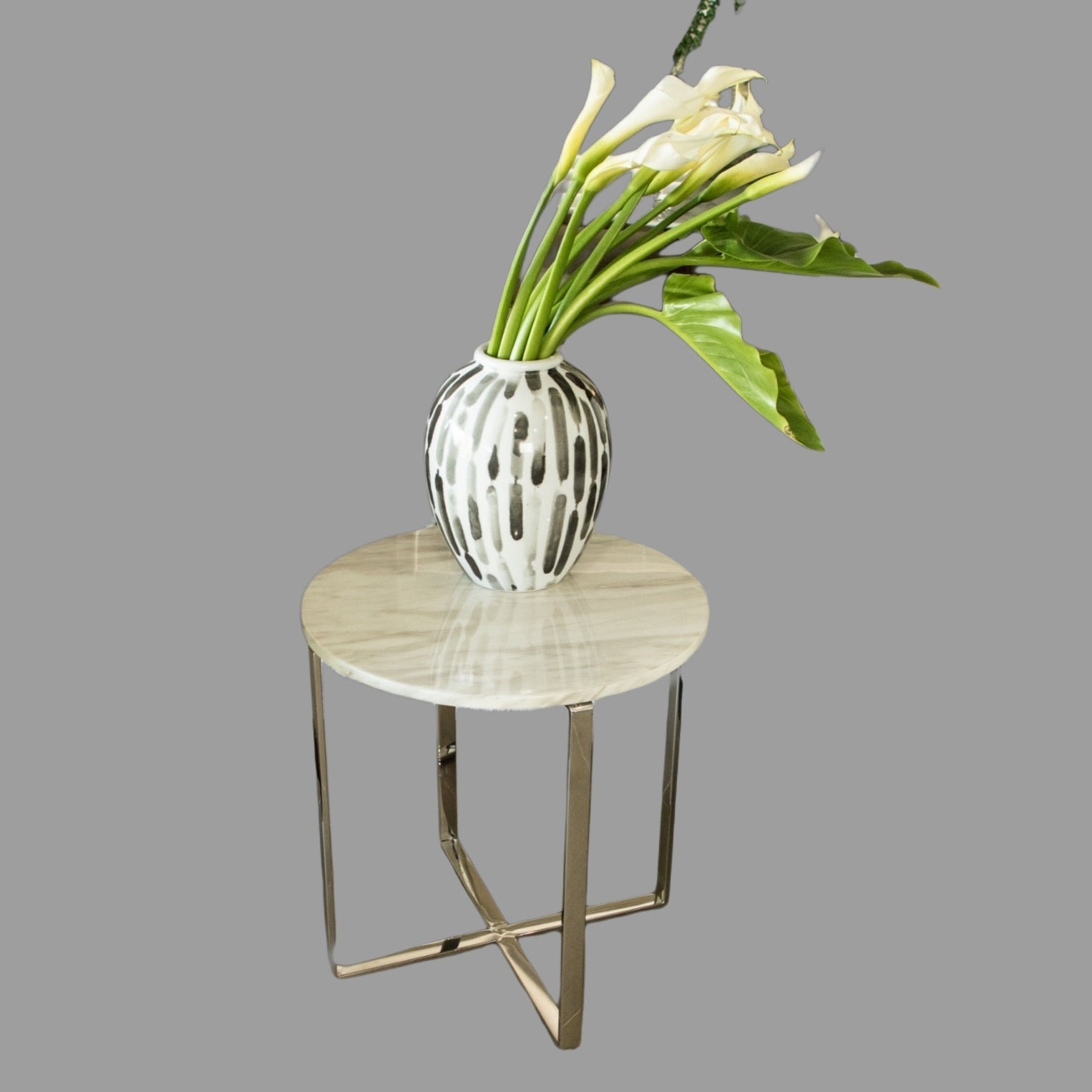 A polished stainless steel side table with a white marble top, displaying a vase with flowers on top.